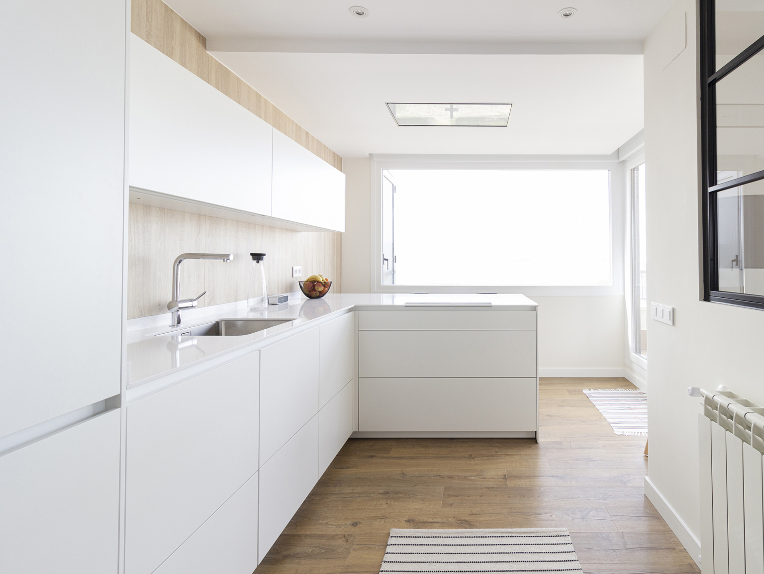 Cocina blanca con península con la placa de cocción incorporada en un proyecto de Santos Vaguada.