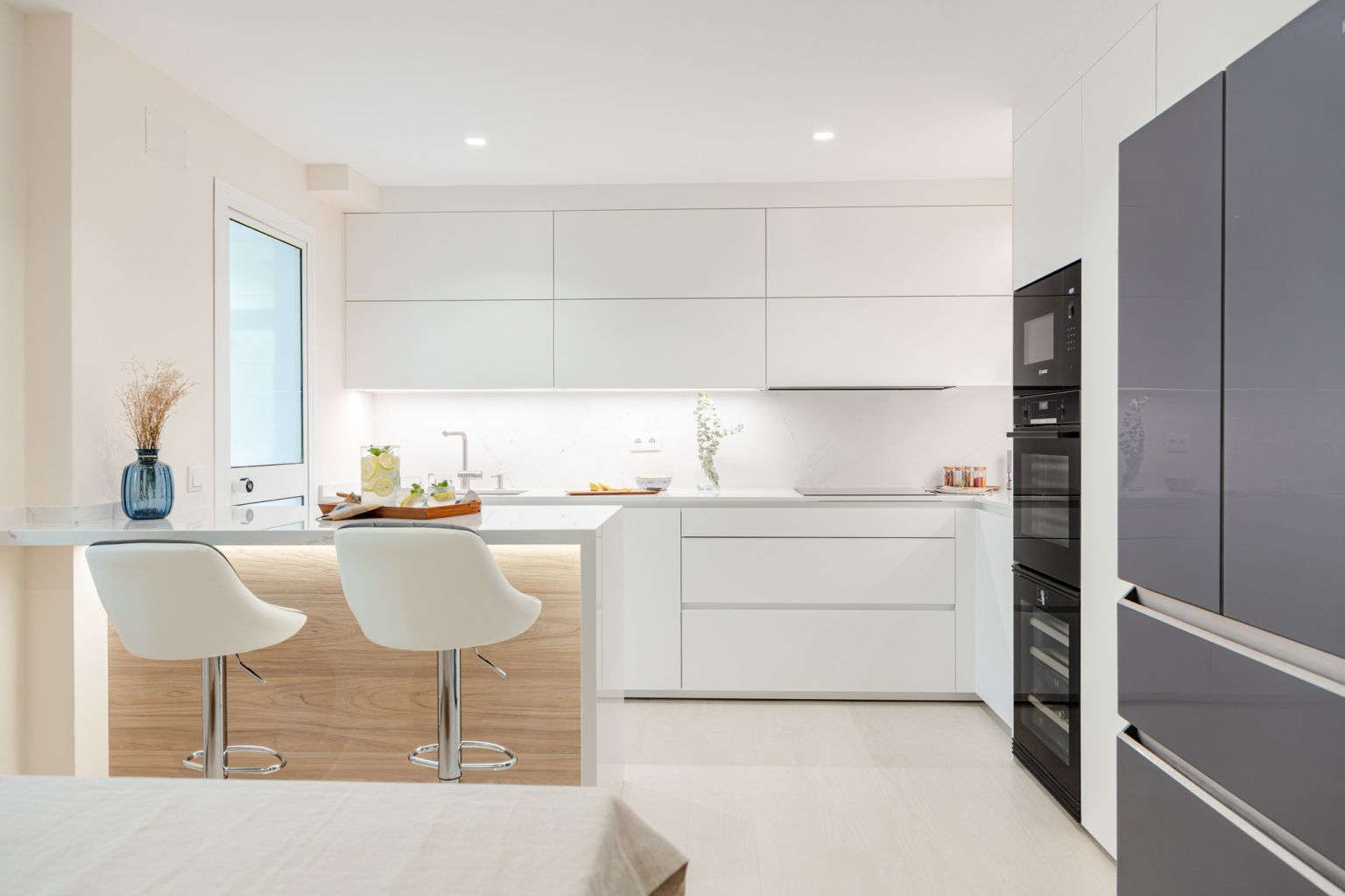 Cocina blanca con península con taburetes diseñada por el estudio Santos Vaguada.